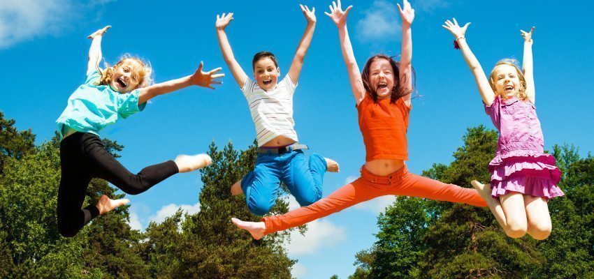 Kids jumping in the air outside on a green meadow.